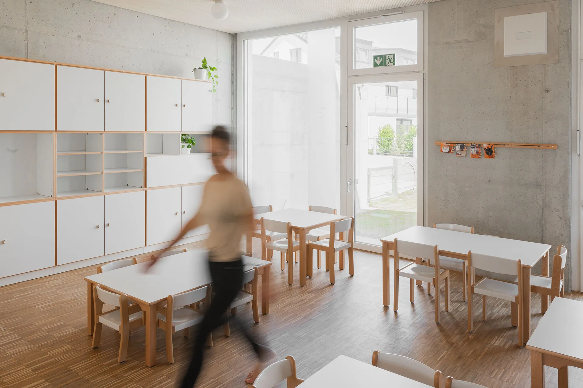 Heller Kita-Gruppenraum mit niedrigen Holztischen, kindgerechten Stühlen und großer weißer Stauraumwand aus modularen Schränken und offenen Regalen von papoq.