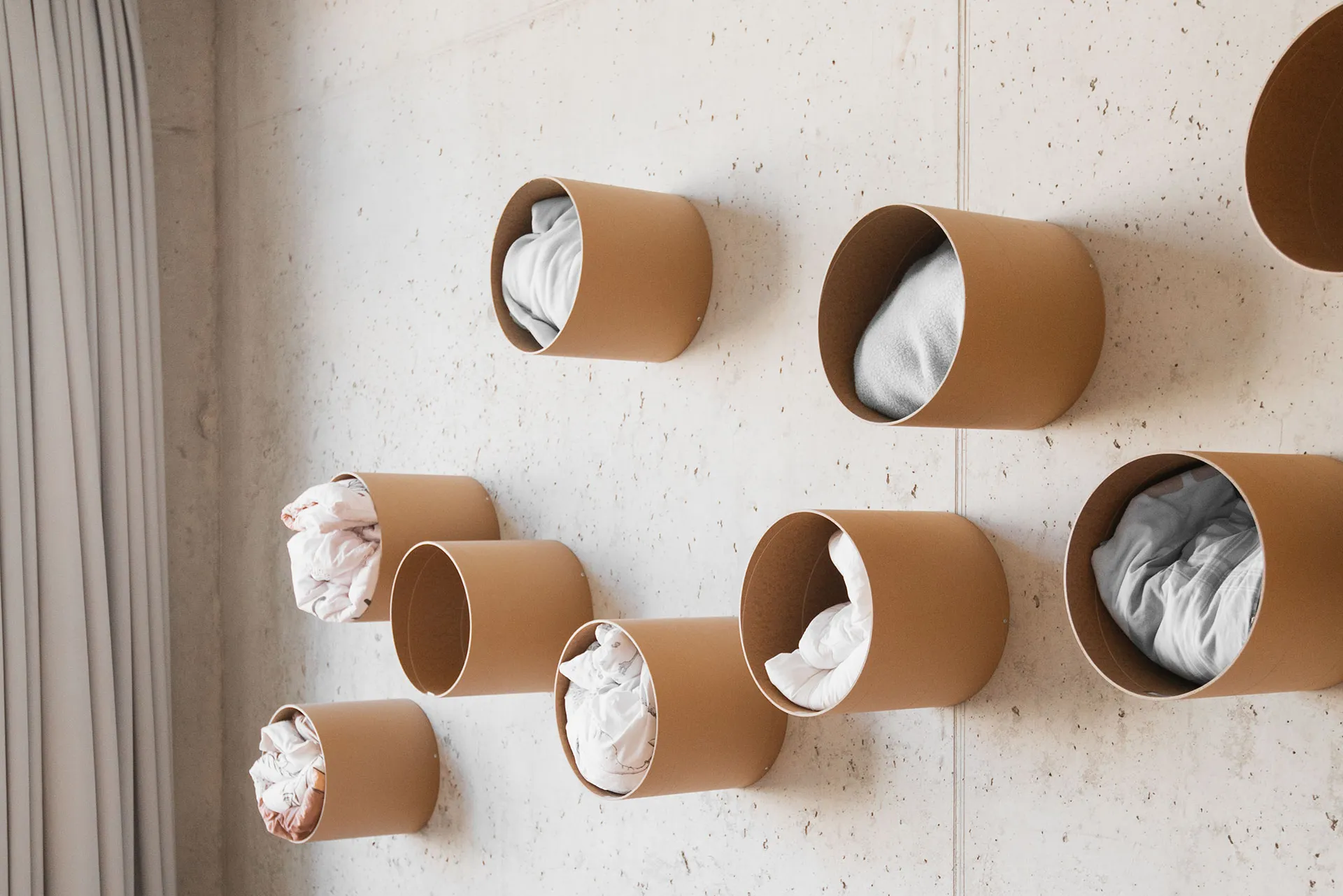 Wandinstallation aus runden braunen Röhren zur Aufbewahrung von Kissen und Bettwäsche im Schlafbereich einer Kita – kreatives Stauraumkonzept von papoq.