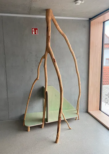 Echter Baumast von der Decke hängend, kombiniert mit einem pastellgrünen Holzpodest als Spielelement für Kinder in der Kita