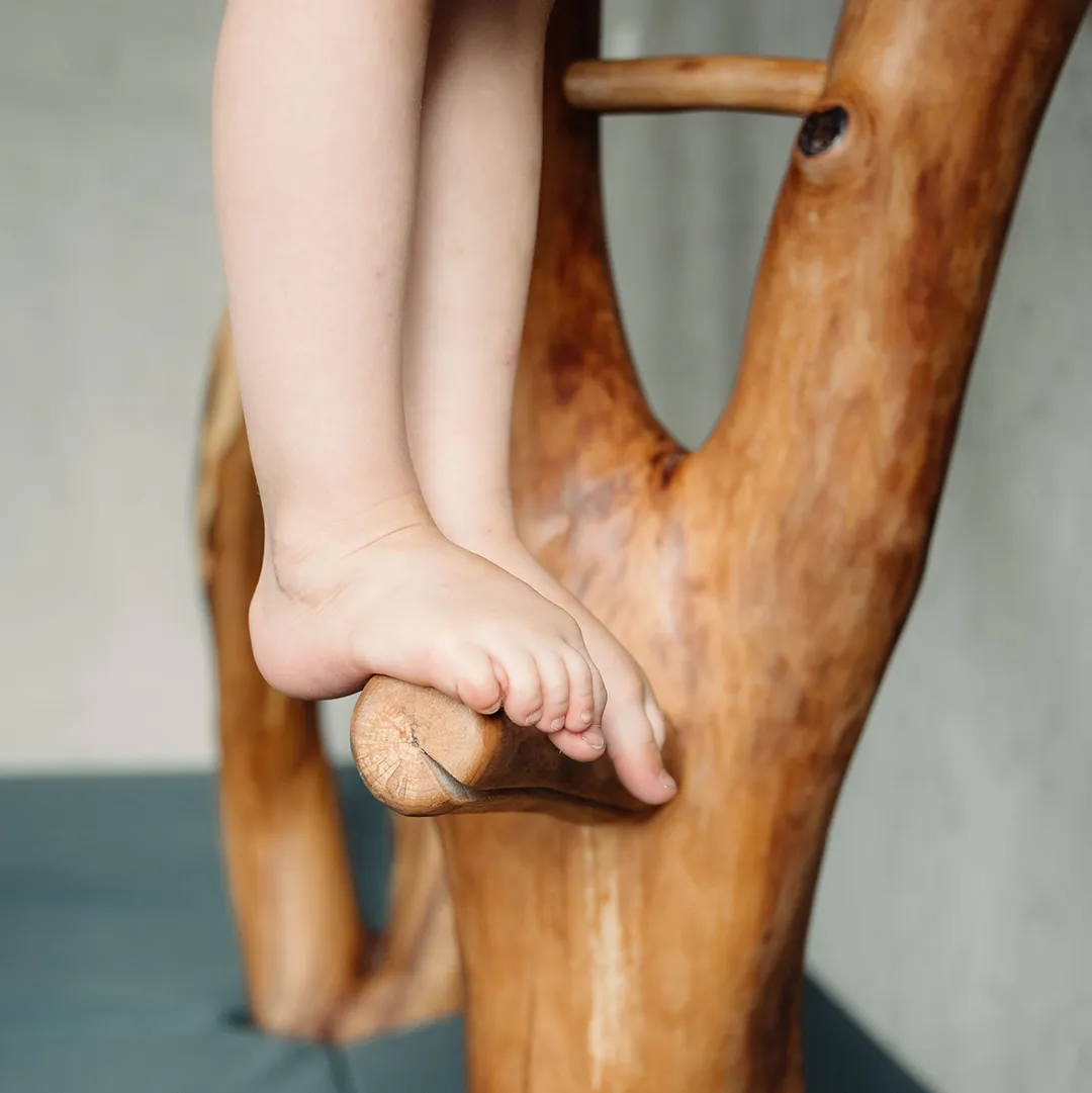 Nahaufnahme nackter Kinderfüße balancierend auf einem dicken Naturholzast