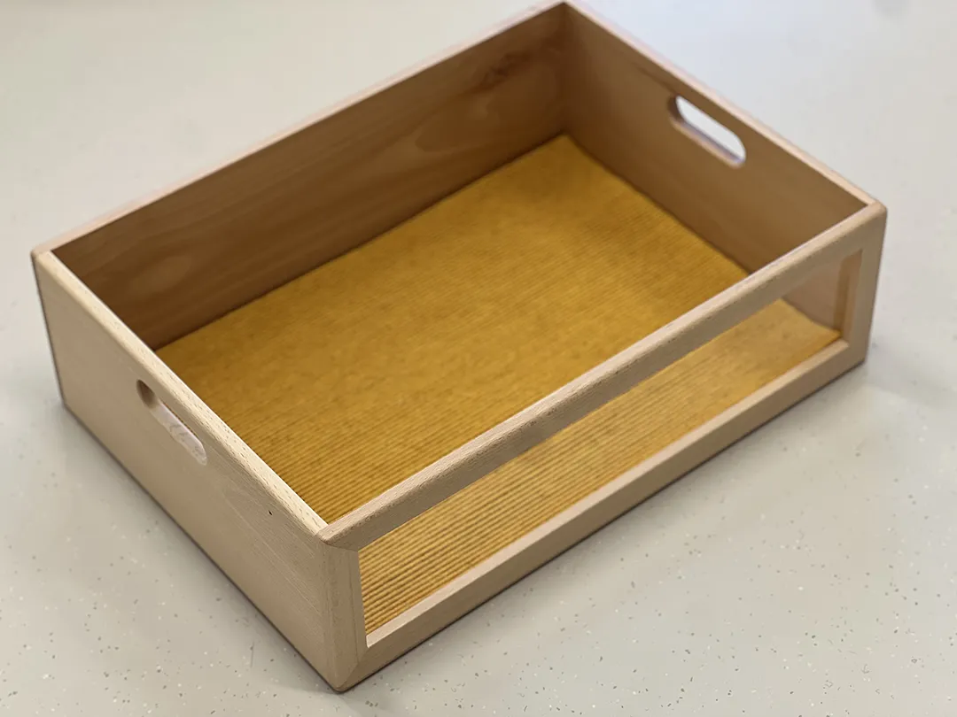 Offene Aufbewahrungsbox aus hellem Naturholz mit gelbem Furnierinnenboden und seitlichen Grifföffnungen
