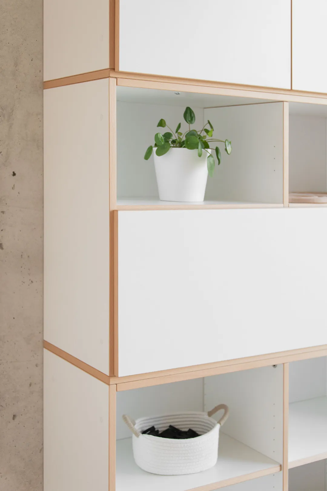 Detailaufnahme eines modularen weißen Kita-Regals mit geöffneter Klapptür, Buchenholzkanten und Pflanze im Fach